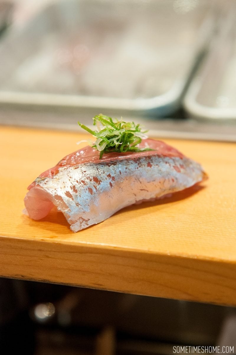 Sushi Dai Restaurant at Tsukiji Fish Market in Tokyo Japan. Photos on Sometimes Home travel blog with a picture of a silvery horse mackerel fish and green scallion. 