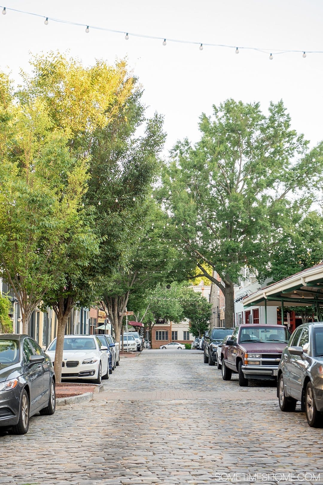 10 Best Downtown Raleigh Photography Spots on Sometimes Home travel blog. Photo of City Market cobblestone street with strung overhead lights.