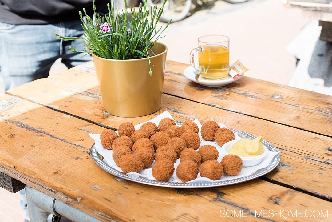 Traditional Dutch foods and drinks to taste in The Netherlands. From Amsterdam desserts to drinks in Holland, cheese in the countryside and more we have your list of snacks and sweets to taste including Herring fish, mini pancakes poffertjes, and stroopwafels. #SometimesHome #TheNetherlands #TraditionalFoods #Dutch #Holland #TypicalCuisine #DutchBeer #DutchFood #AmsterdamArea
