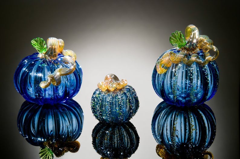 Three glass pumpkins against a black background with lighting.