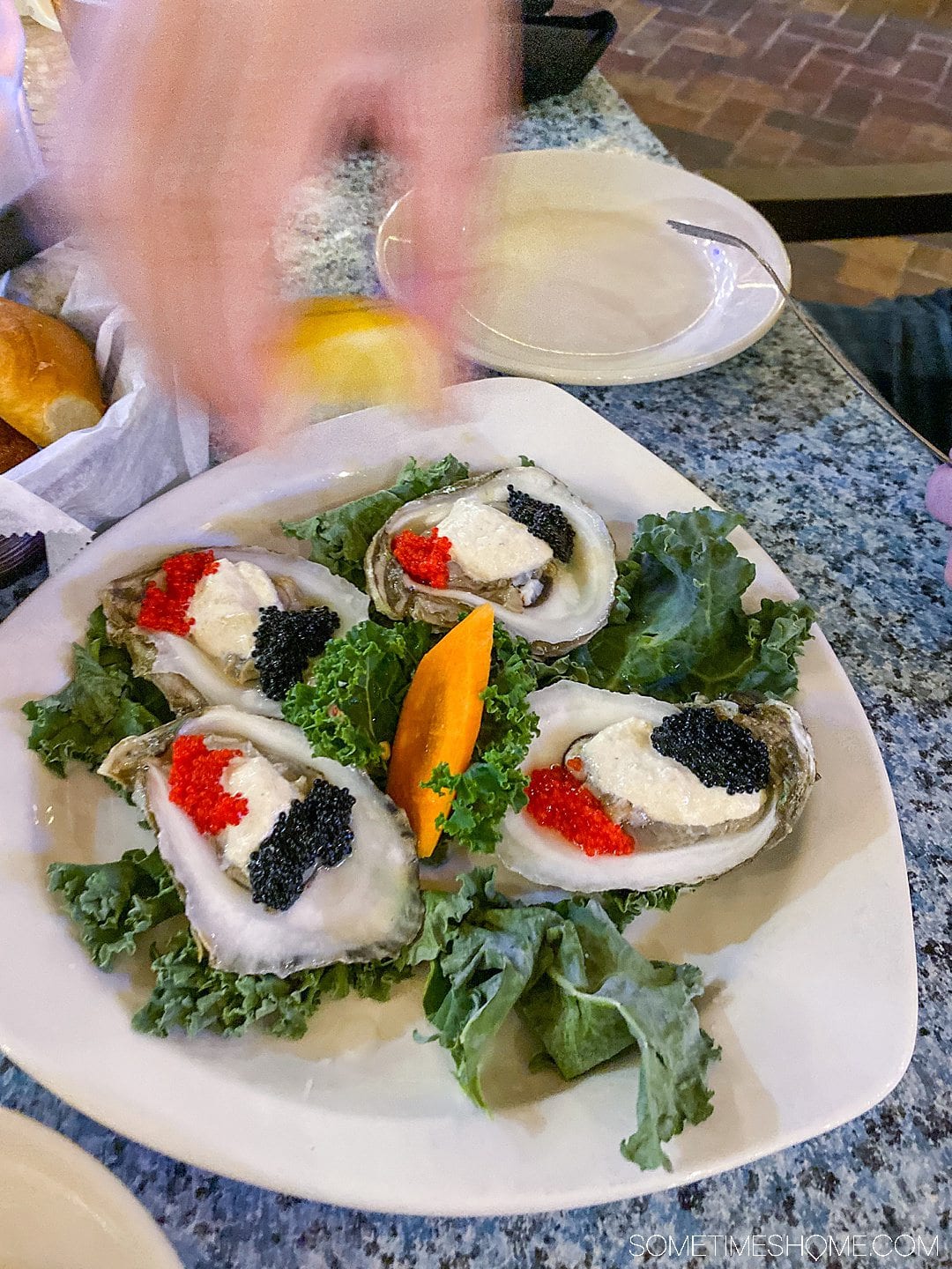 A place of four oysters and a hand in motion squeezing a lemon above the plate.