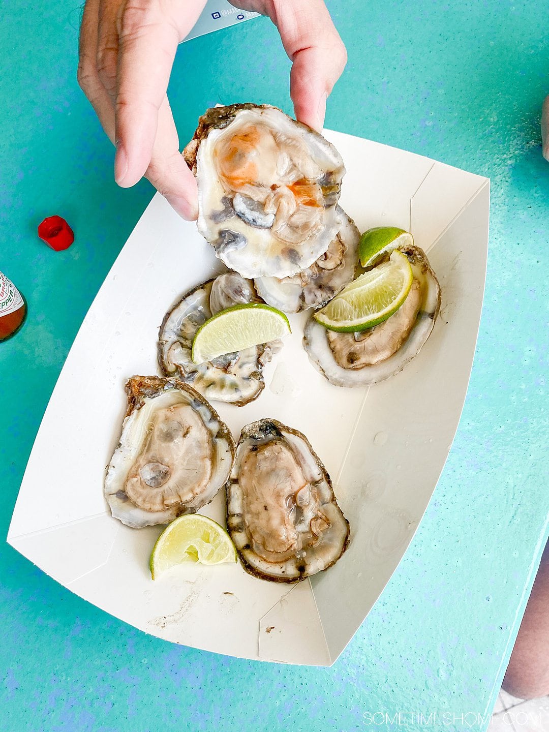 6 oysters with a paper tray, and a man holding one of them.