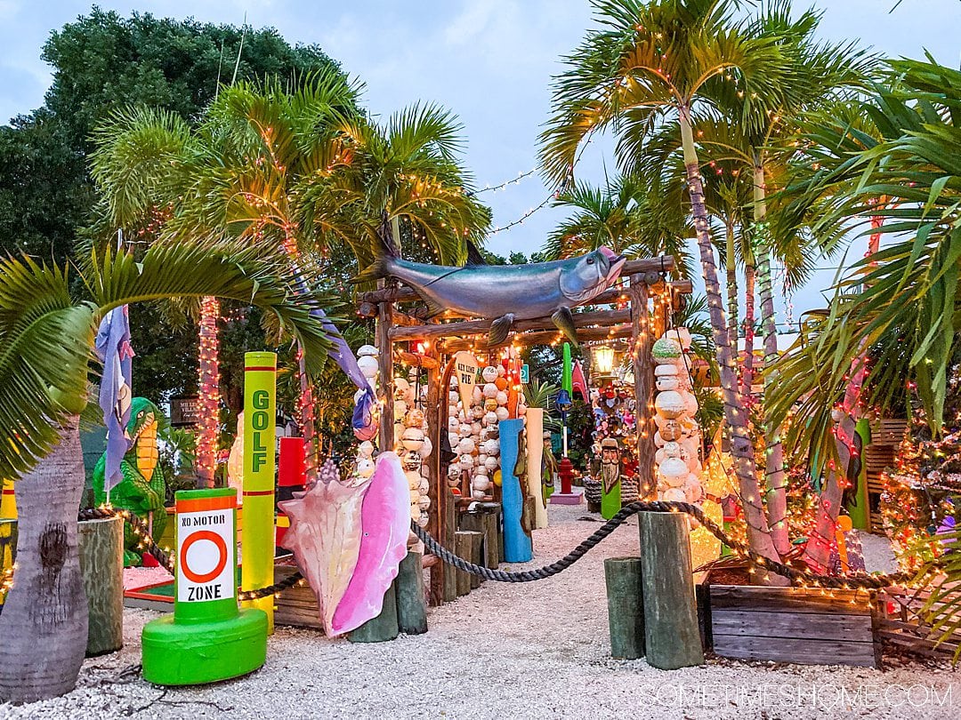 Palm trees and lights at dusk at an outdoor spot with an eclectic collection.