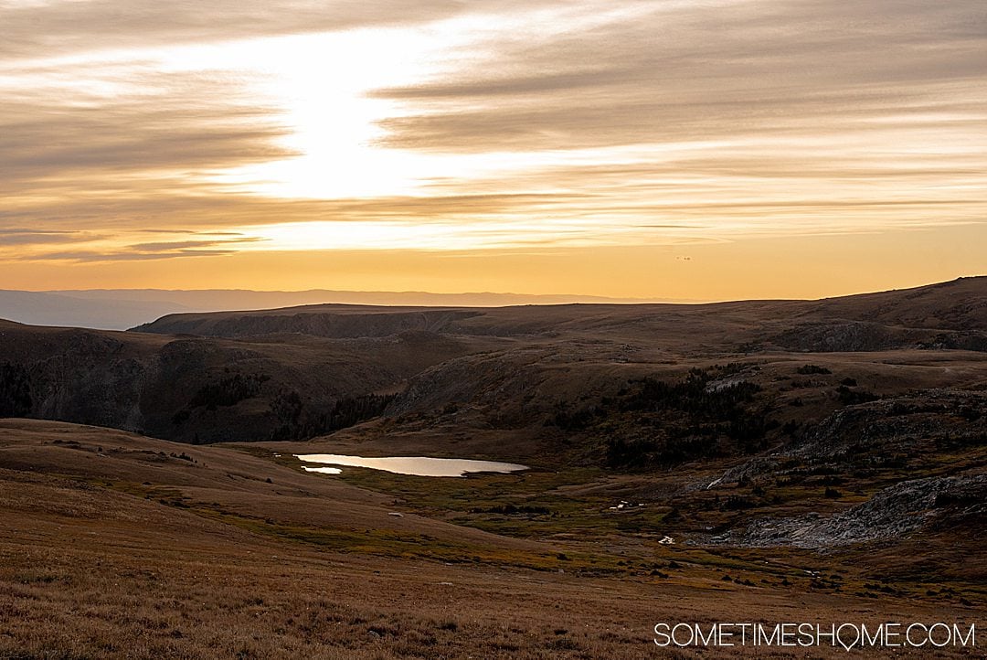 Apus de soare reflectând pe un lac în depărtare de autostrada Beartooth în Montana, cu siluetele munți întunecați.