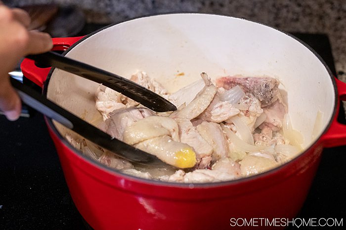 Chicken, onions and grapes in a red pot for a chicken recipe.