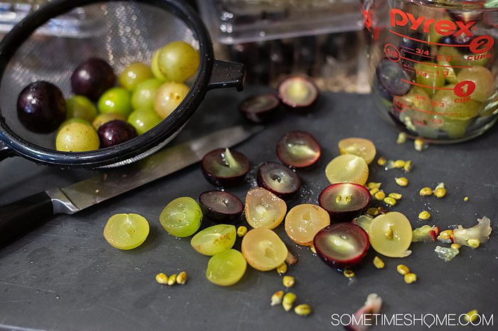 Green and red grapes cut in half on a black cutting board for a Muscadine chicken recipe.