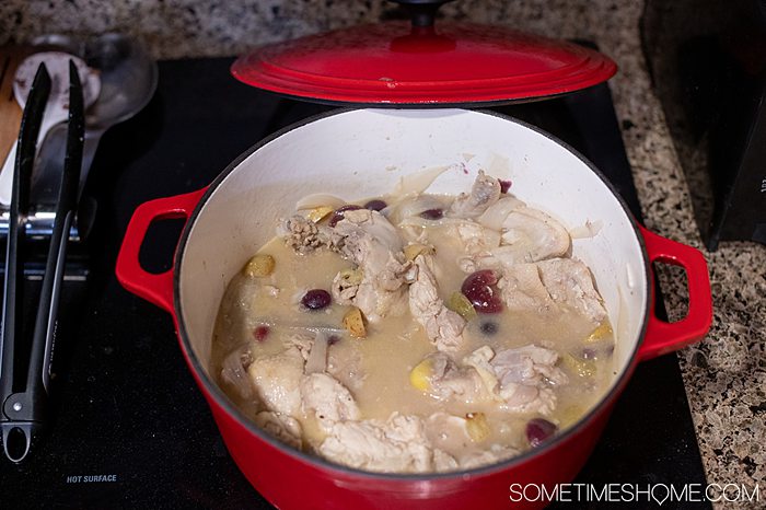 Chicken, grapes and broth cooking in a red pot on an electric glass stove top.