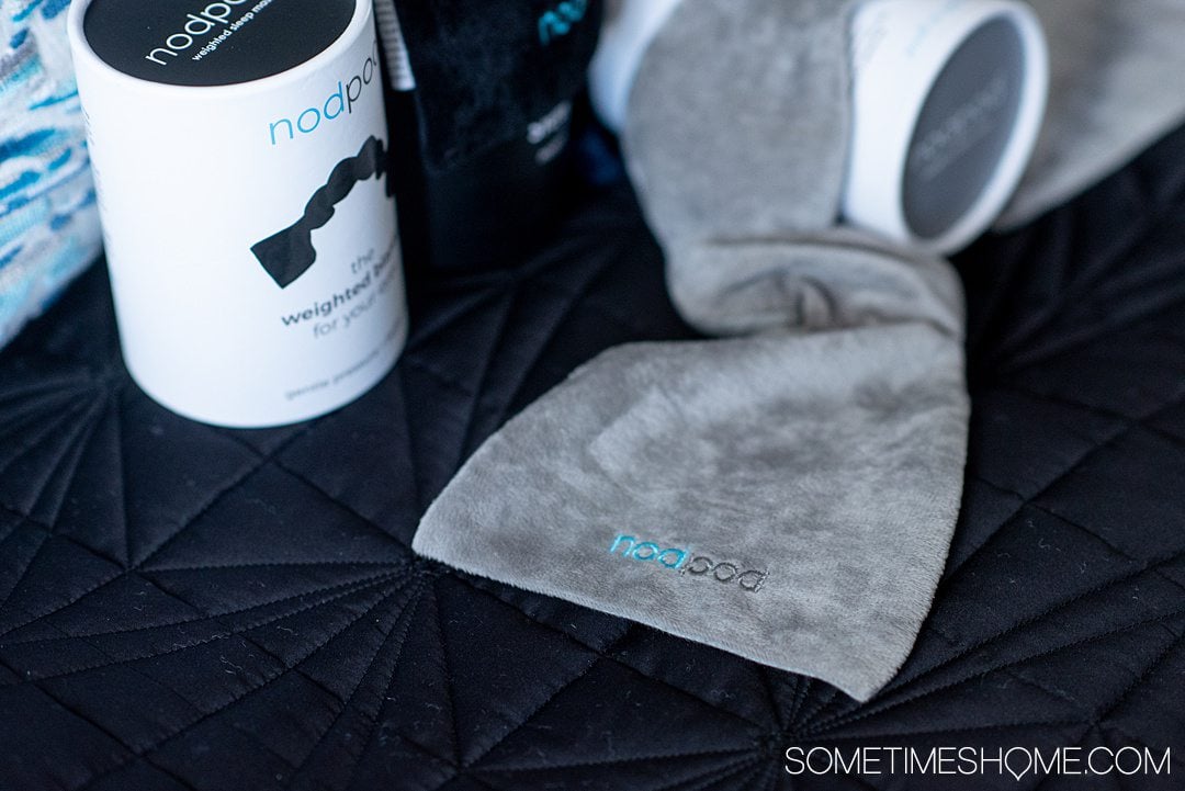 nodpod eye masks in grey and black on a blue pillow.