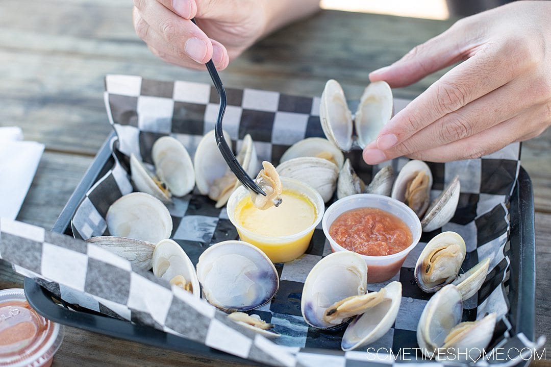 A plate of steamed clams and a man holding one and a fork in the other hand.