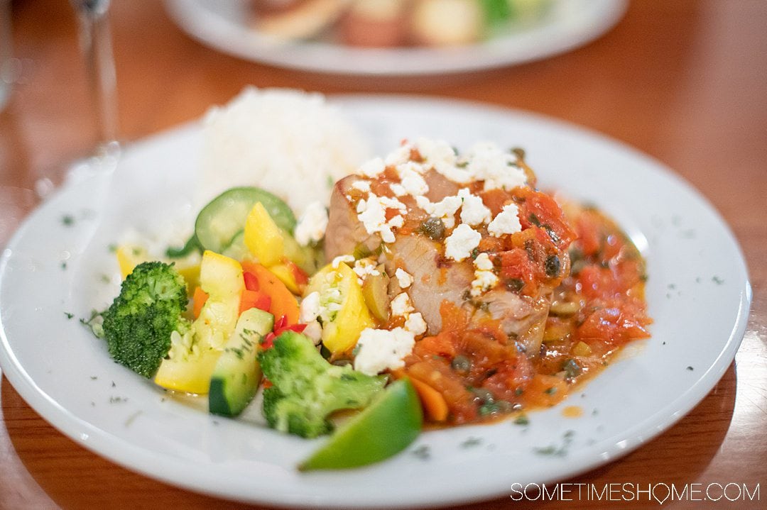 A plate of steamed vegetables and a Mediterranean sauce on top of a piece of fish.