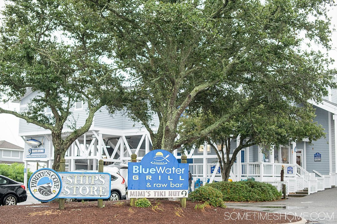 Trees and a restaurant behind it. A sign out front reads, "Blue Water Grill & Raw Bar" in the Outer Banks.