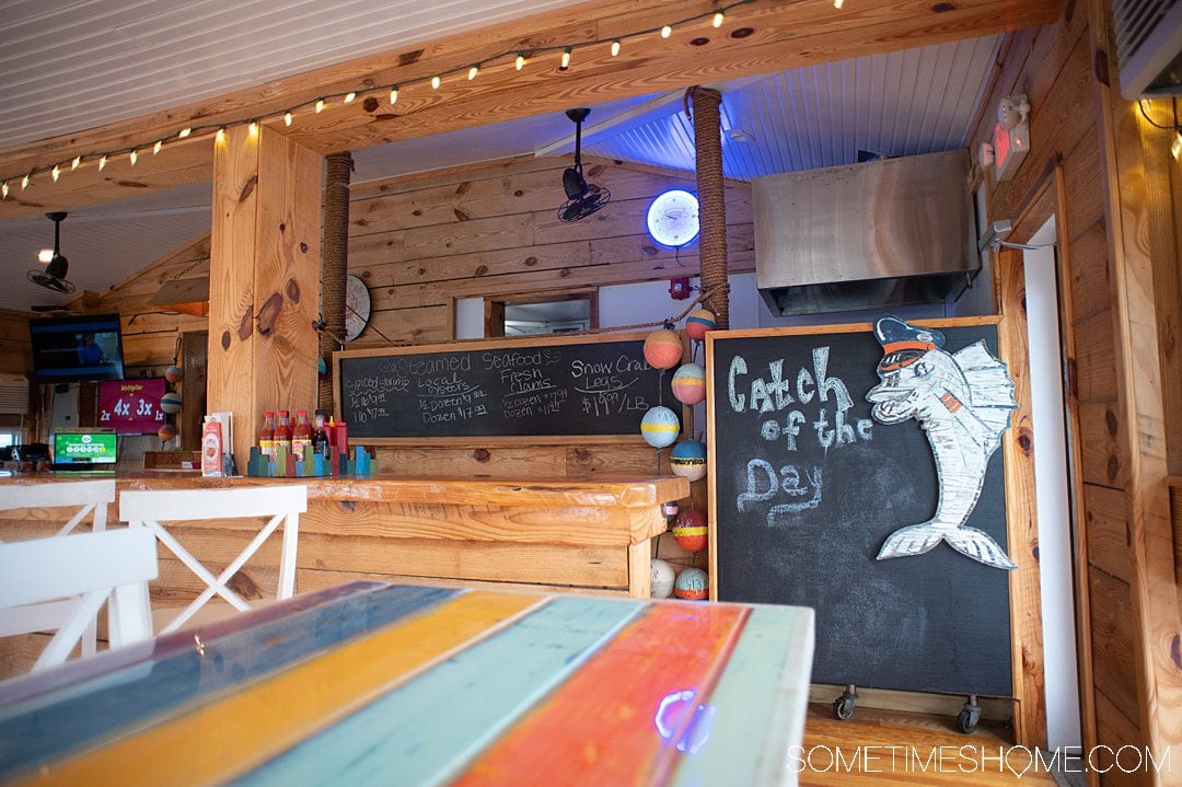 Colorful interior of a restaurant with "Catch of the Day" written on the blackboard and a characterized fish next to it. Buoys are the left of the board at this best seafood restaurant in the Outer Banks.