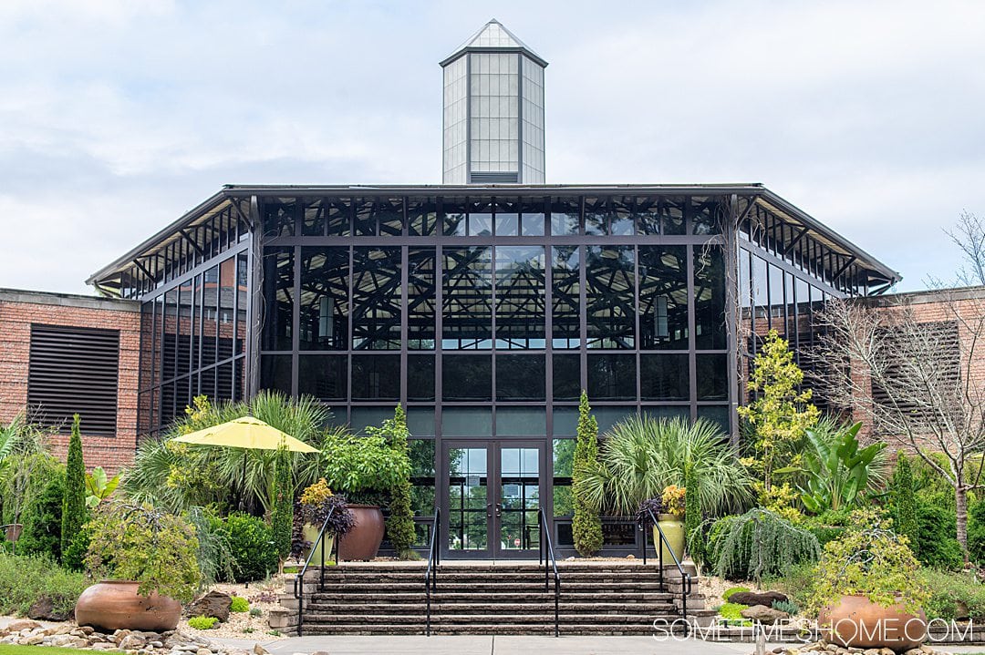 Glass facade of the main building at Cape Fear Botanical Gardens in Fayetteville, NC, surrounded by plants.