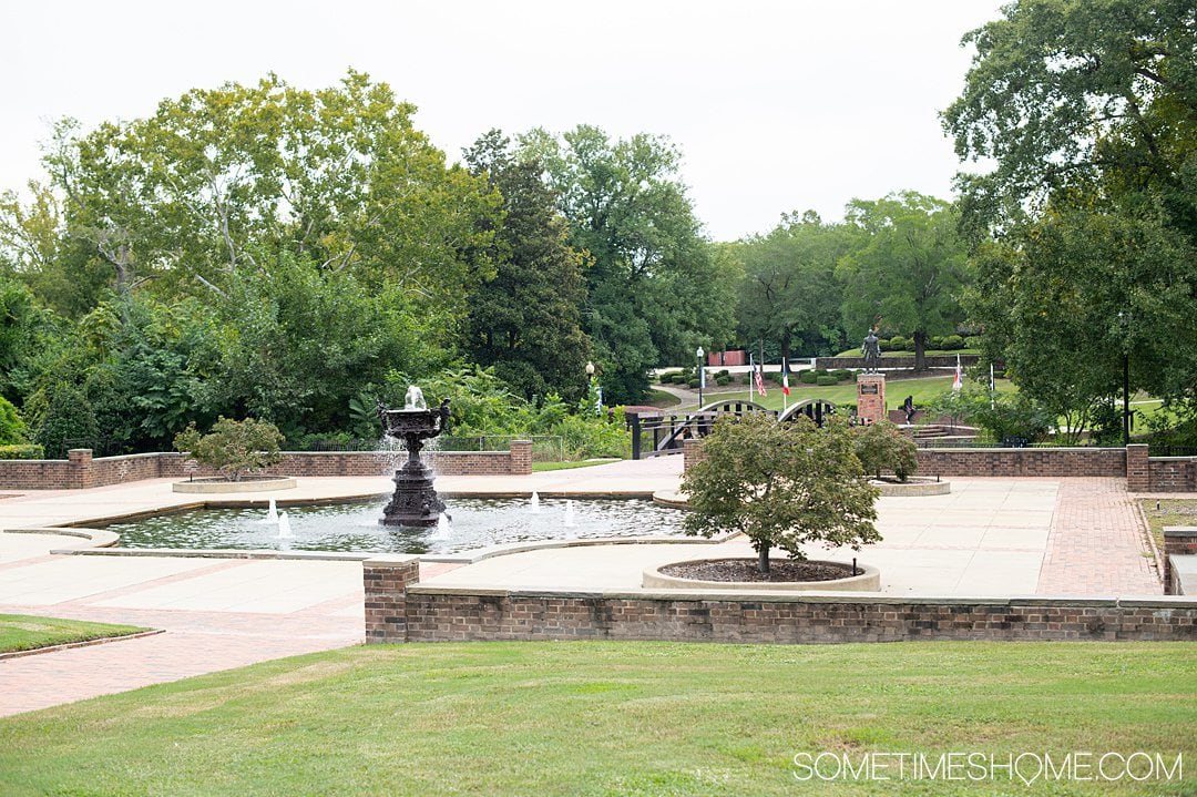 View of a park fountain and green grass and trees in Fayetteville, NC.