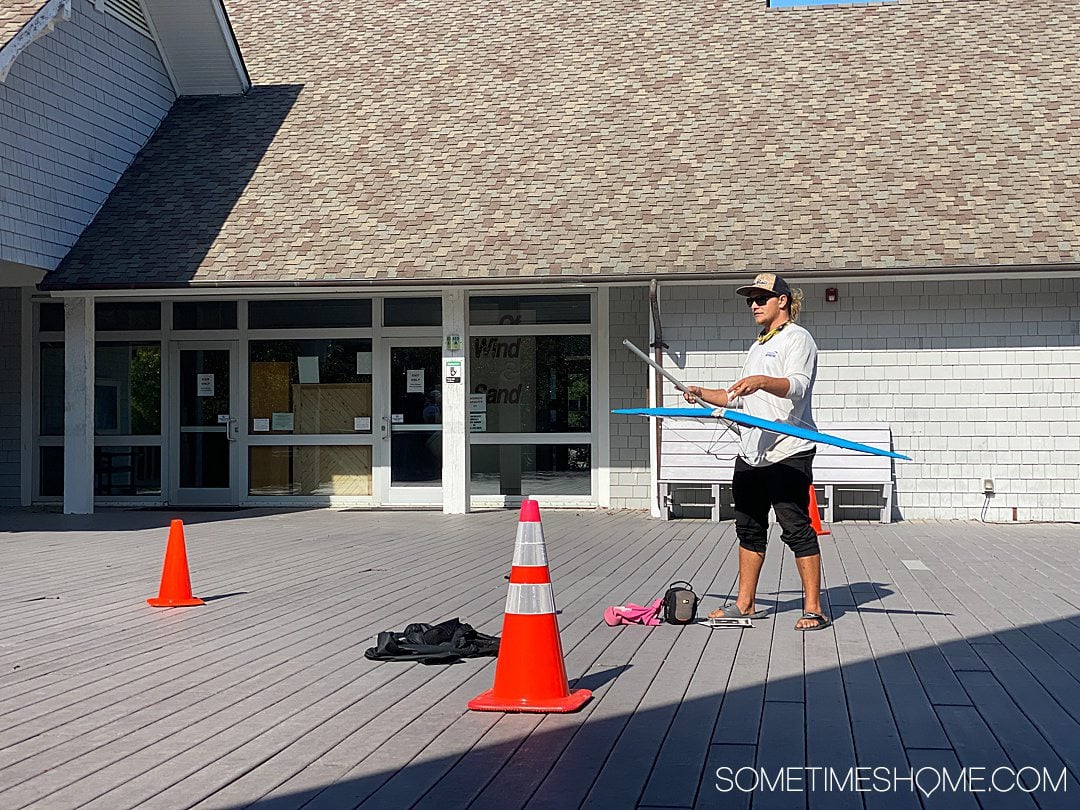 Image of a man with a small hang glider model and two orange traffic cones on a grey balcony for a Hang Gliding in the Outer Banks post.