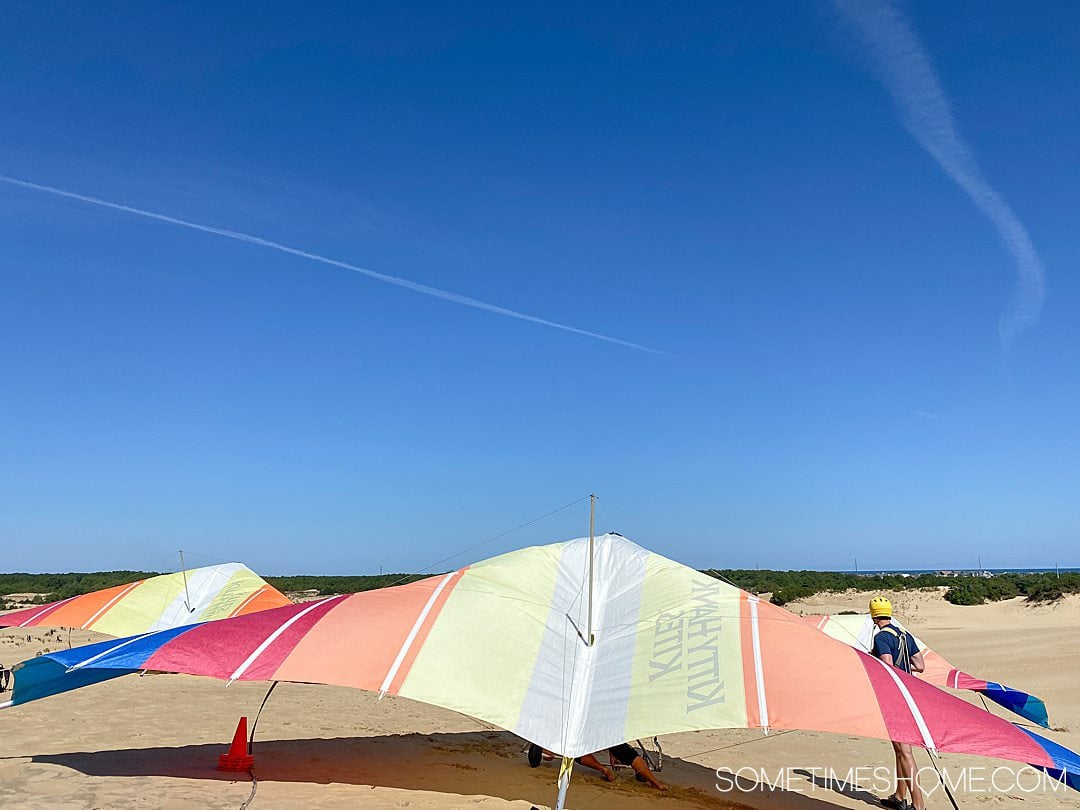 Hang gliding in the Outer Banks of NC with colorful red, yellow and blue hang gliders and tan colored sand dunes and blue sky at Jockey's Ridge State Park in Nags Head.