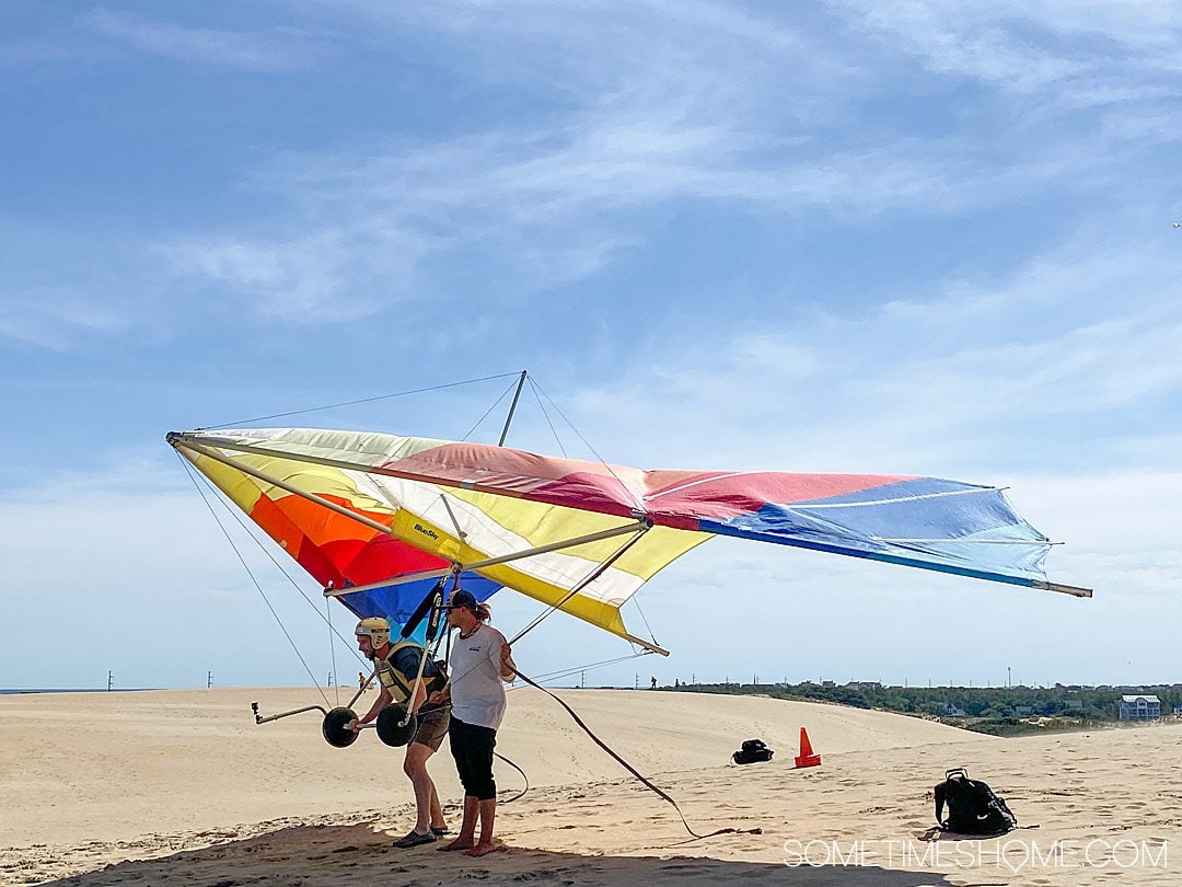 Colorful hang gliders and people with tan colored sand dunes and blue sky at Jockey's Ridge State Park in Nags Head, of the Outer Banks in NC.