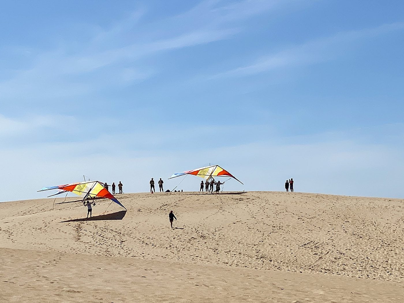 Hang gliding in the Outer Banks of NC with colorful red, yellow and blue hang gliders and tan colored sand dunes and blue sky at Jockey's Ridge State Park in Nags Head.