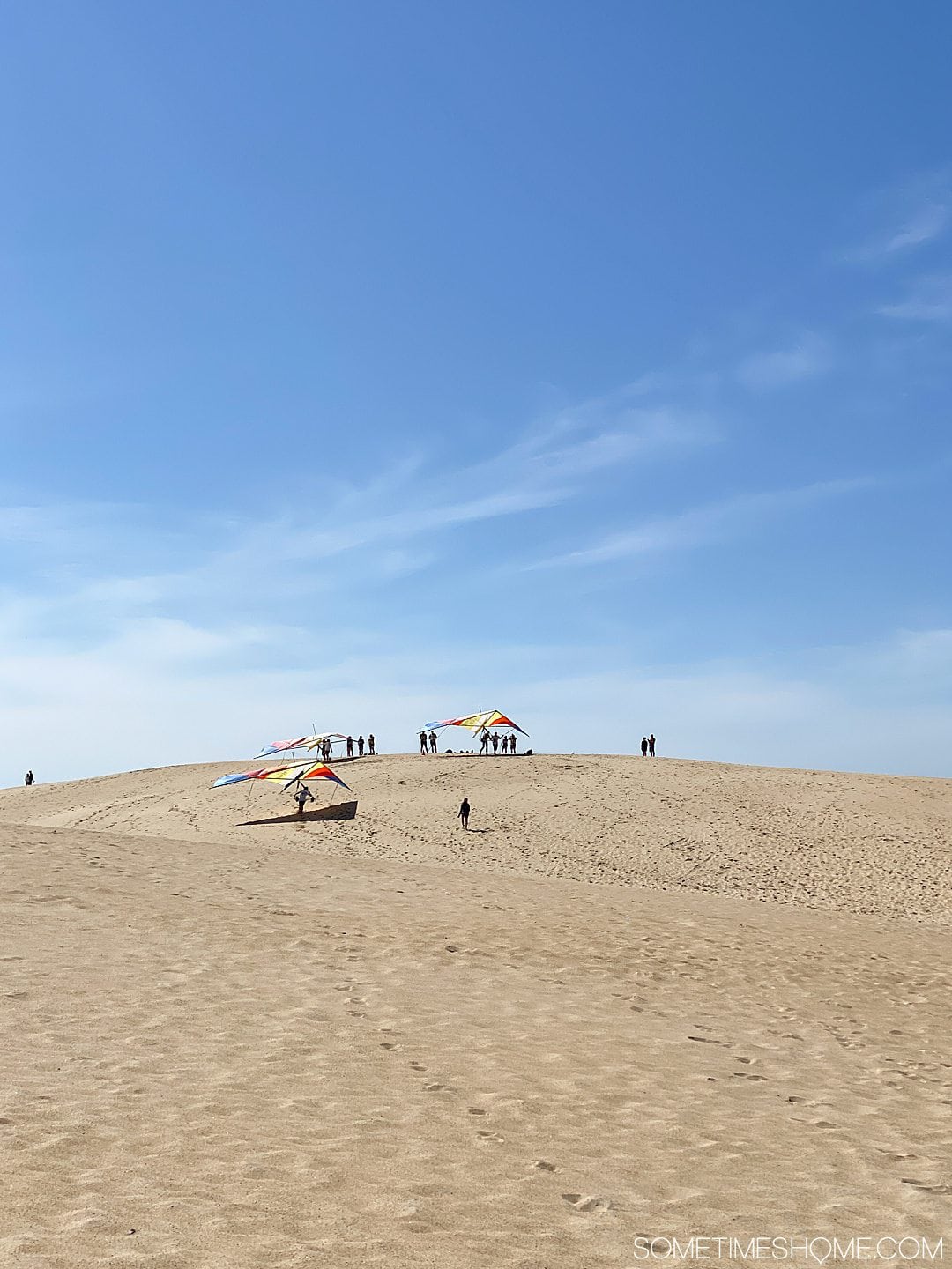 Hang gliders and people in the distance with tan colored sand dunes and blue sky at Jockey's Ridge State Park in Nags Head, of the Outer Banks in NC.