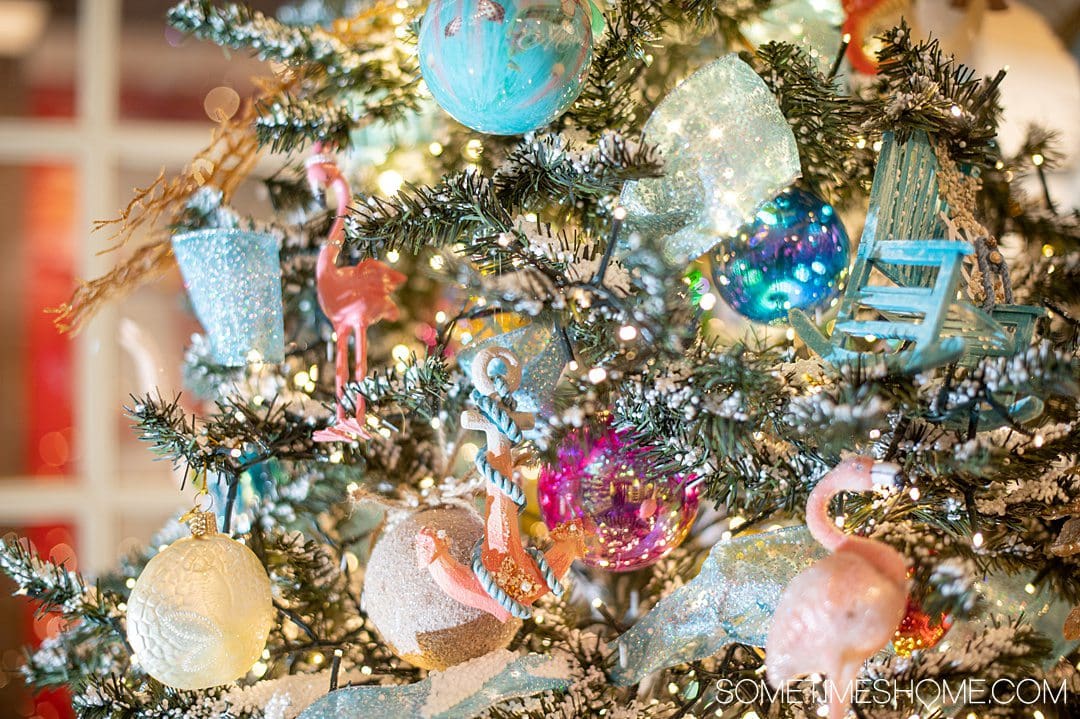 Close up photo of holiday ornaments, including blue, peach and pink pieces, on a colorful holiday tree.