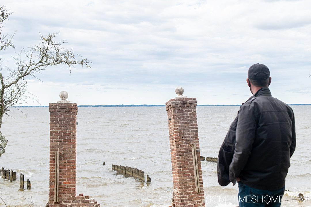 A man looking out to the water and two square brick pillars on Roanoke Island at the Elizabethan Gardens in the Outer Banks.