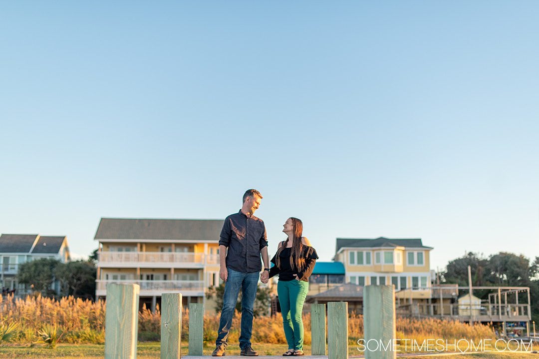 A couple on a dock with a yellow painted hotel in the distance, and golden hour during sunset at the Inn on Pamlico Sound in the Outer Banks in October in Buxton, NC.