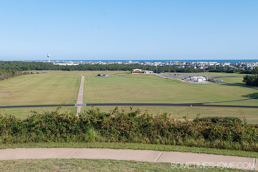 Bird's eye view looking down at a grassy field out to the water with a blue sky, in the Outer Banks at Kill Devil Hills.