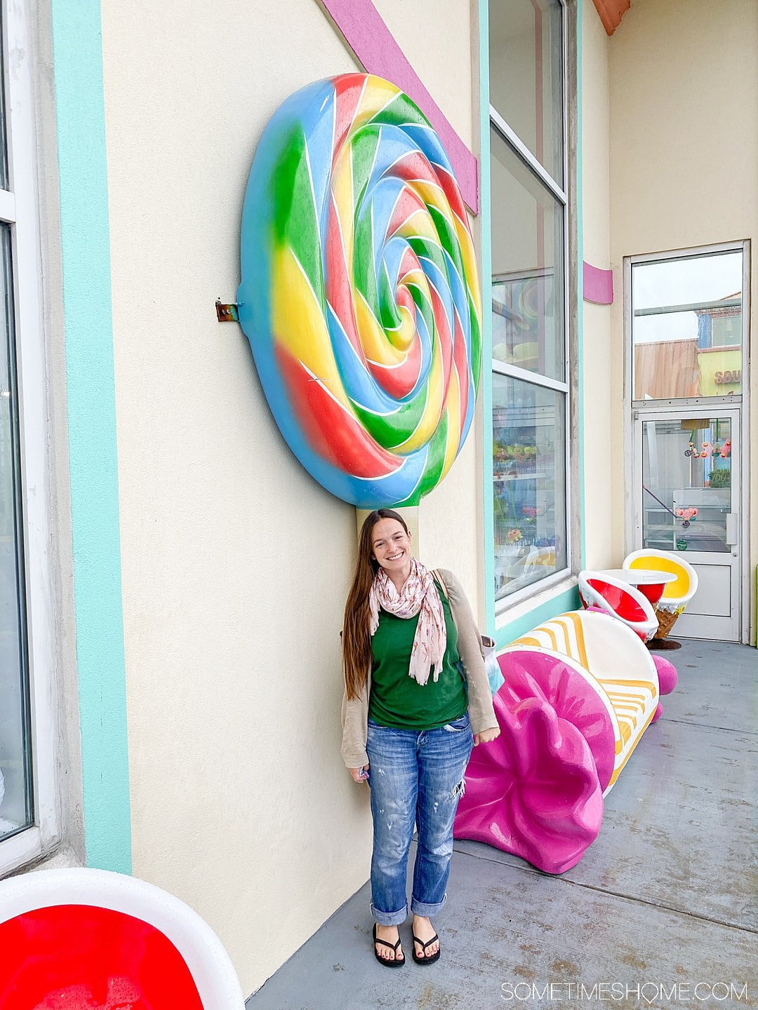 A woman standing in front of a colorful, oversized rainbow swirl lollipop in the Outer Banks of North Carolina.