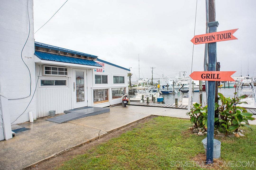 Signage at a waterfront restaurant at a marina to the white-painted restaurant with a blue roof.