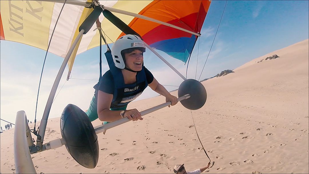 A woman hang gliding with a blue helmet on in the Outer Banks.