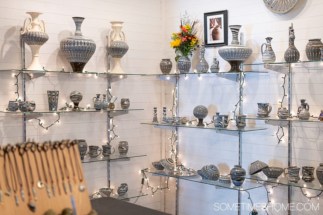 Pottery pieces on glass shelves against a white wall for Seagrove Pottery in NC.