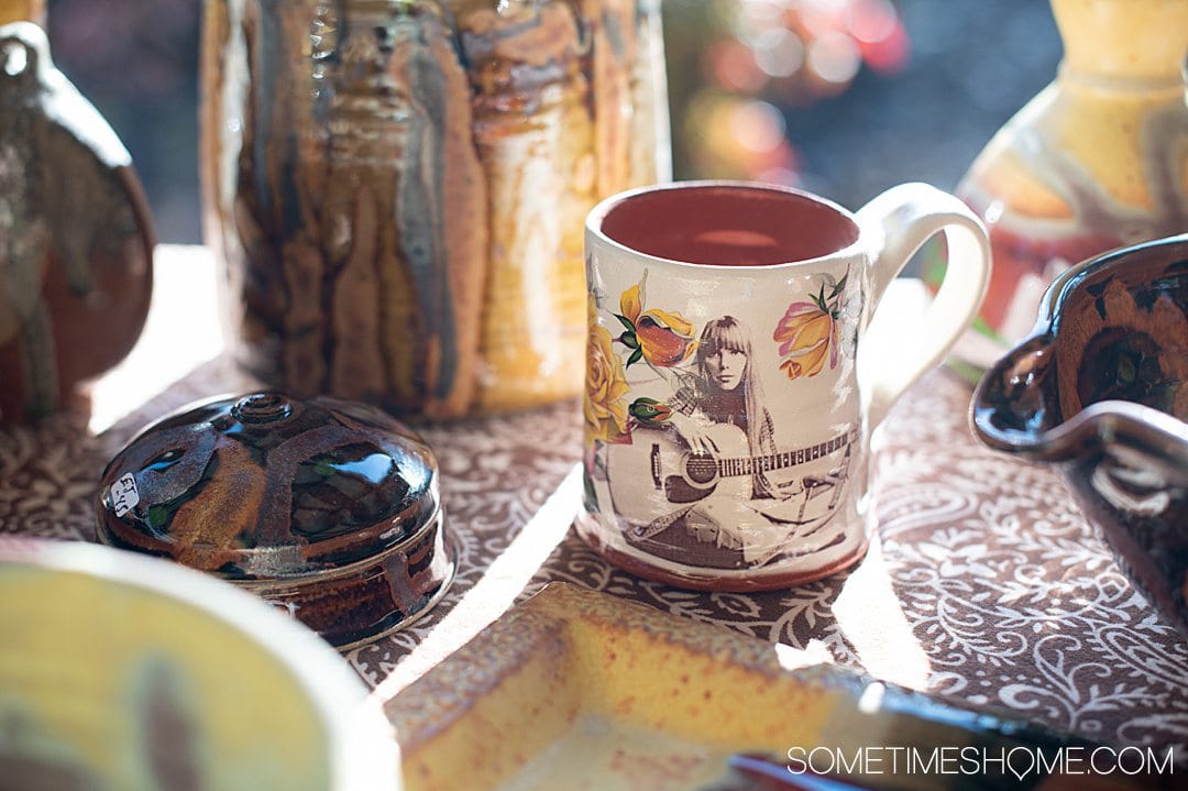 Handmade pottery mug painted white with yellow flowers and Joni Mitchell playing the guitar on it by Stephanie Martin, Seagrove pottery.