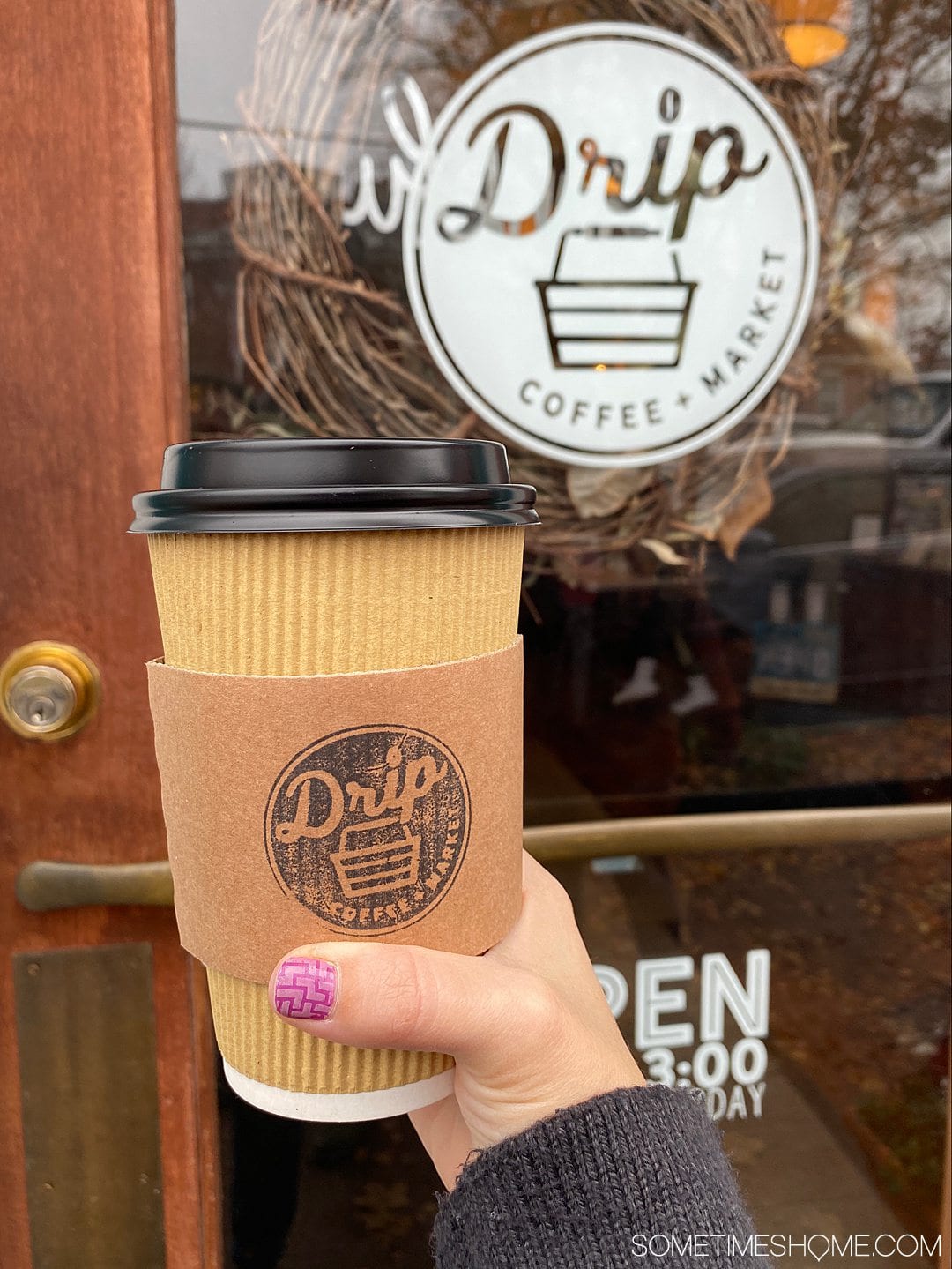 Female hand with a pink painted nail holding a coffee cup.