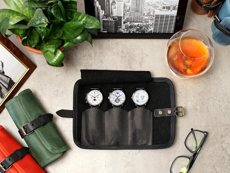 Watch roll with three watches, glasses nearby and a glass of bourbon from an overhead view.