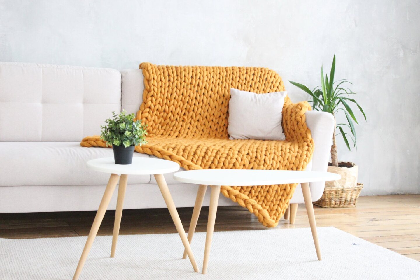 Yellow chunky knit throw blanket on a white couch with white tables in front of it via Etsy.