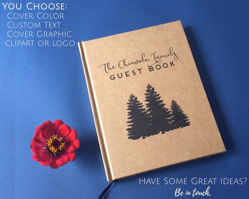 Custom handmade journal with silhouettes of three evergreen trees on kraft paper against a blue background for unique house warming gift ideas.