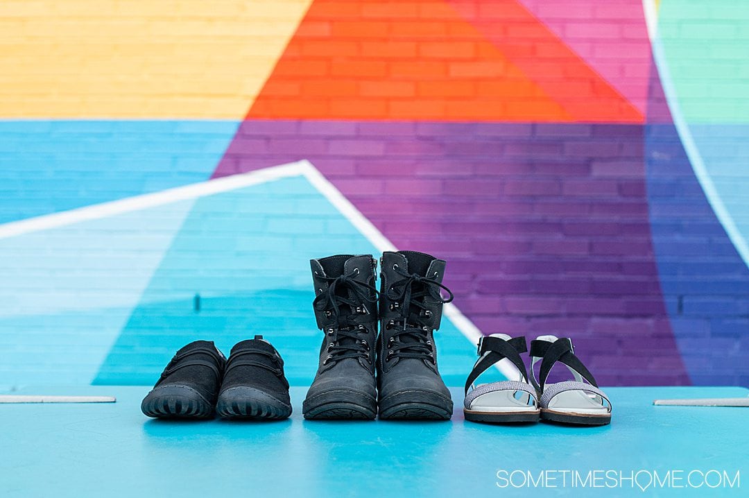 Three pairs of women's Jambu & Co. shoes in a row, in black, against a colorful background.