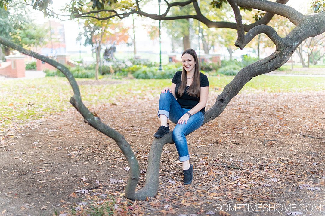 Women sitting on a tree branch in jeans and a black top, with Jambu & Co. pair of Ashton flat black shoes on.