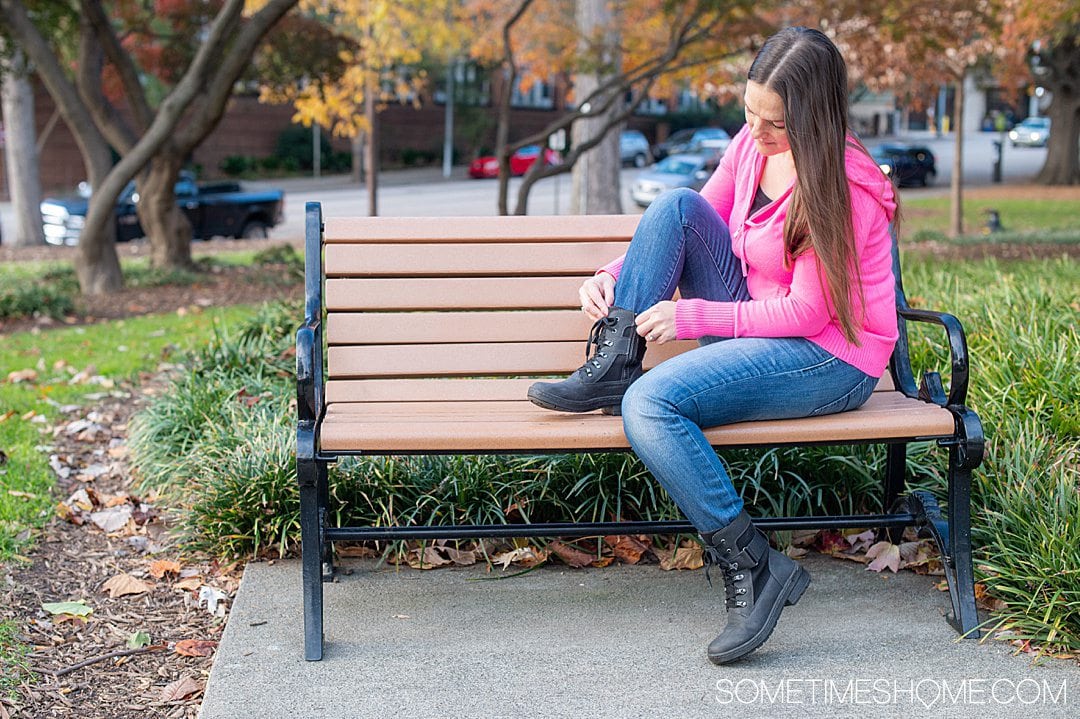 Woman sitting on a bench in blue jeans and a hot pink sweater hoodie with black combat-boot inspired shoes on from Jambu & Co.