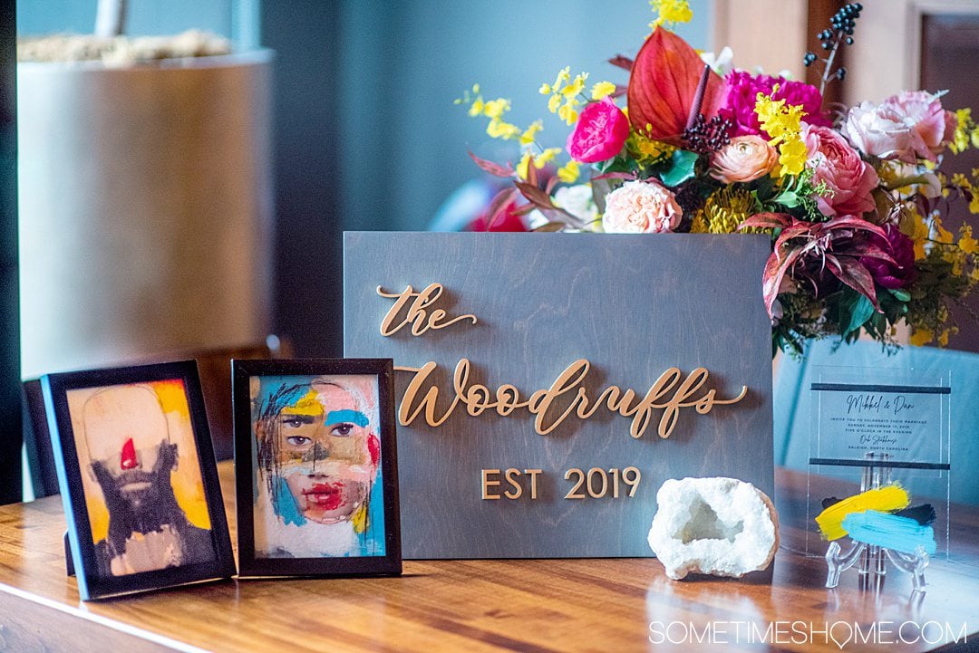 Grey and gold wooden sign with a couple's last name and Est. 2019 with flowers and frames around it.