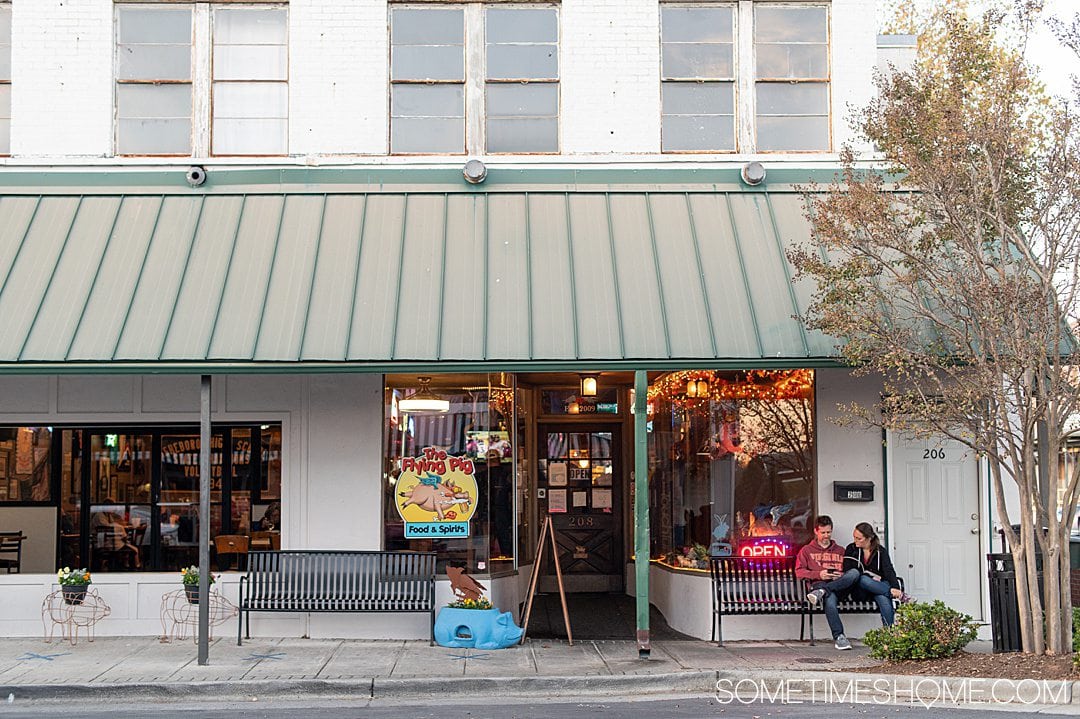 Front of a restaurant with a green awning, called The Flying Pig in downtown Asheboro, NC.