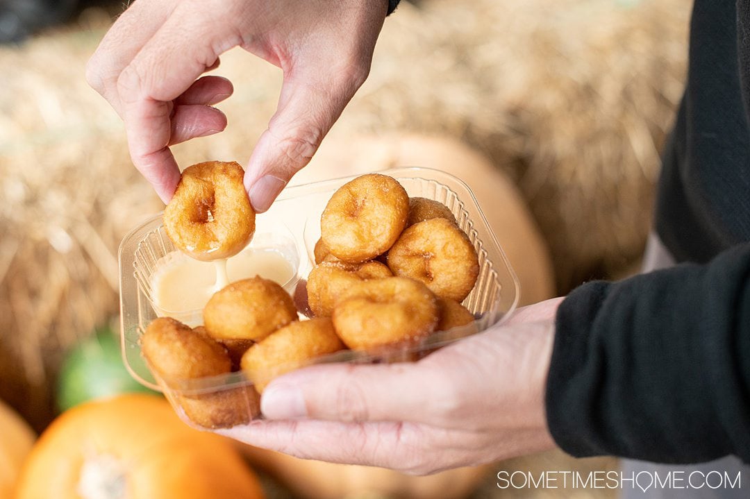 A man's hand dunking mini donuts in a sauce.