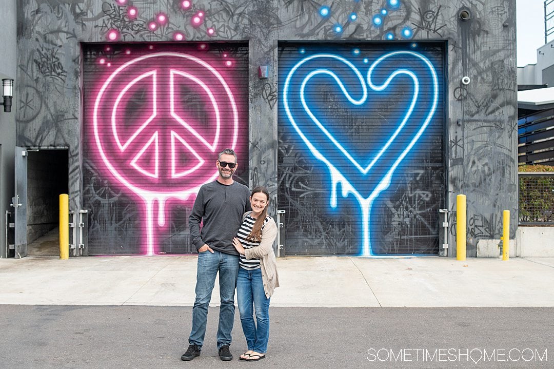 A couple in front of a peace sign and heart mural.