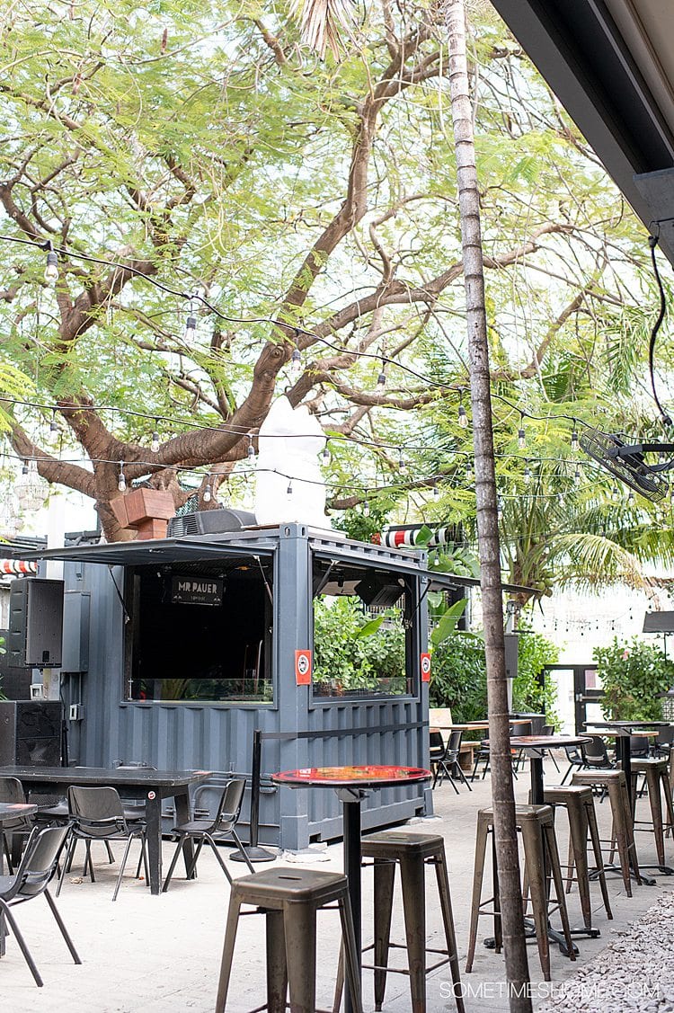 Outdoor patio of 1-800-Lucky in Wynwood, Miami in Florida with a grey kiosk and tables outside.