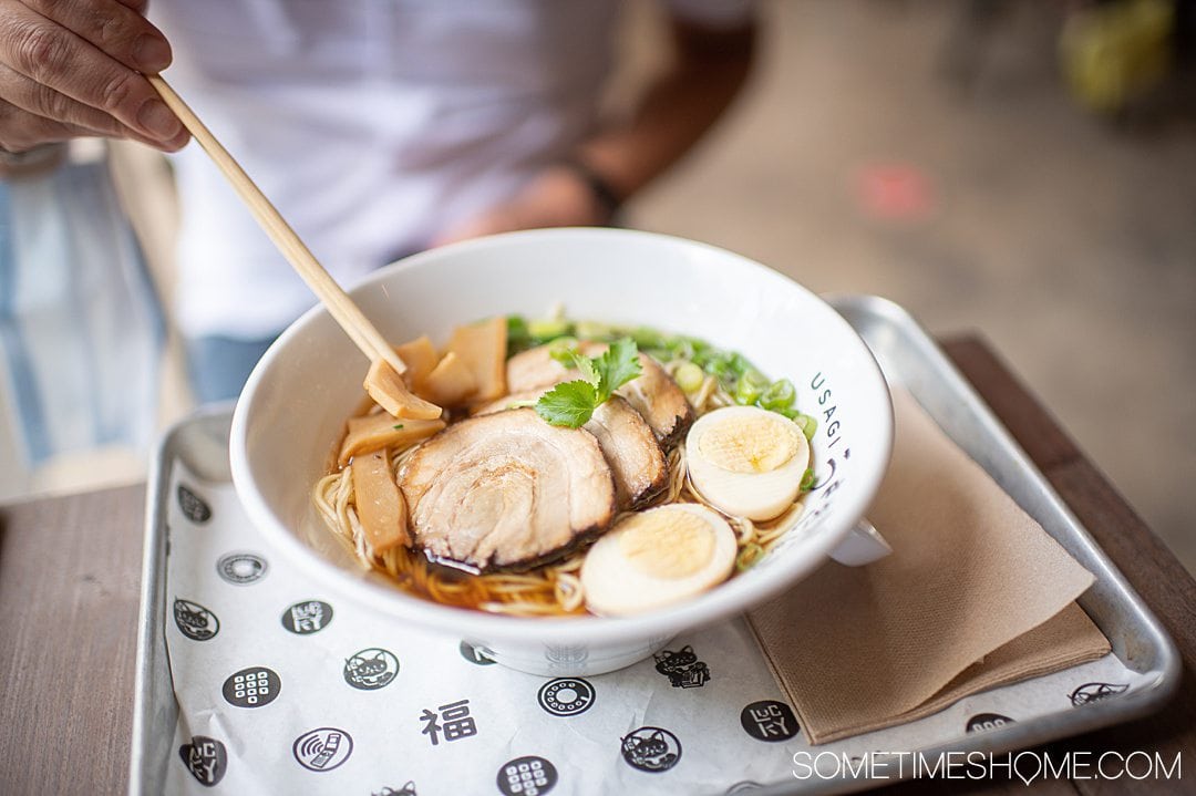 A bowl of tonkatsu ramen with an egg, meal, green onions and chopsticks on the left at 1-800-Lucky in Wynwood, Miami, FL.