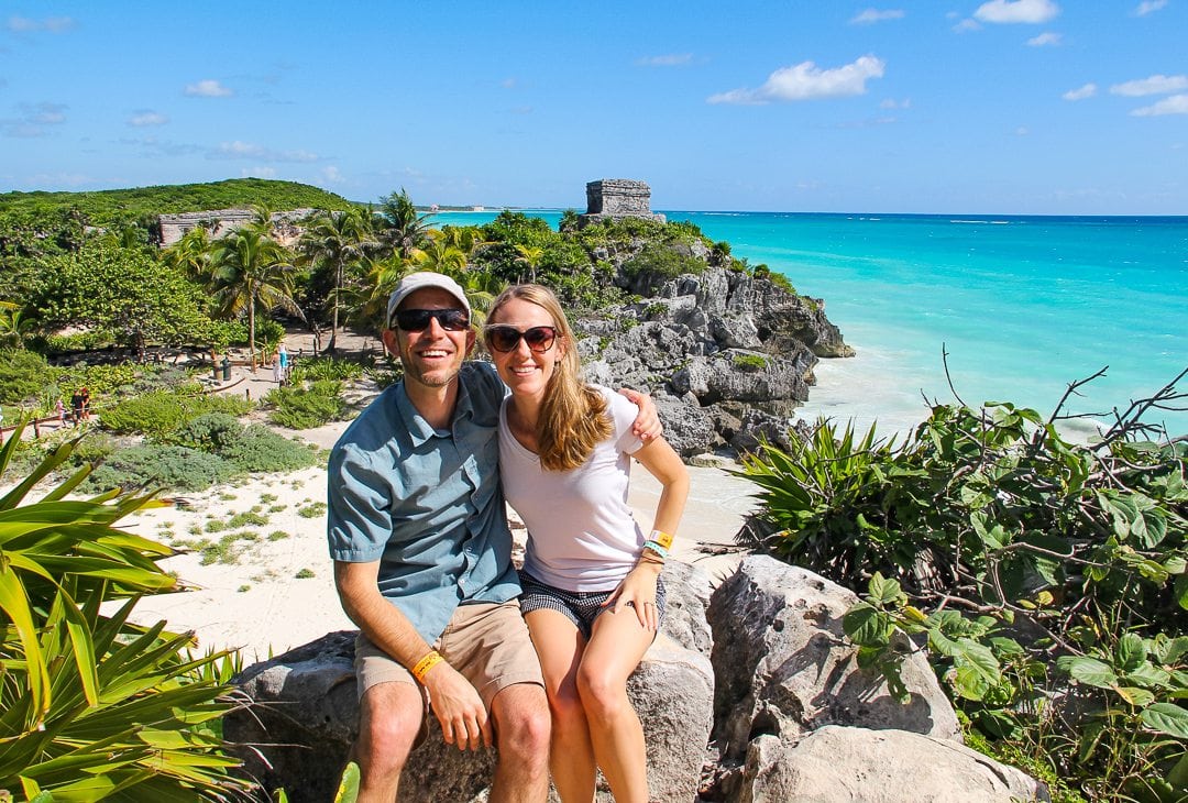 Couple sitting on a rock with blue water and landscaping behind them.