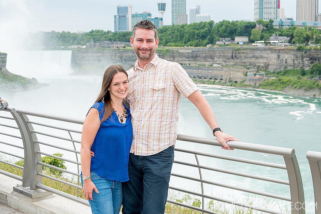 Couple travel bloggers, a female and male, standing in front of Niagara Falls during summer.