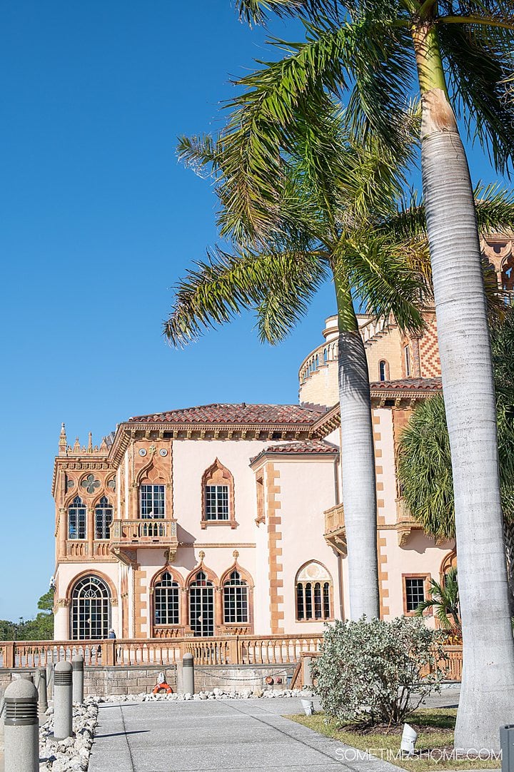 Light pink home on the waterfront with blue skies and palm trees, called Ca' d'Zan at The Ringling in Sarasota, FL.