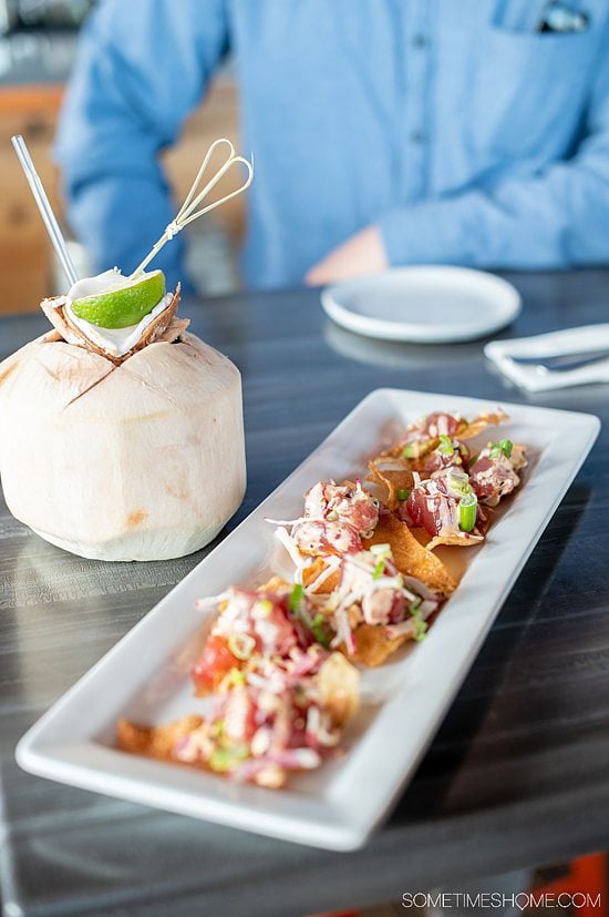 A rectangular plate with tuna-topped nachos and a coconut drink next to it with a straw and a lime at Spice, a restaurant in Fort Mill, SC.