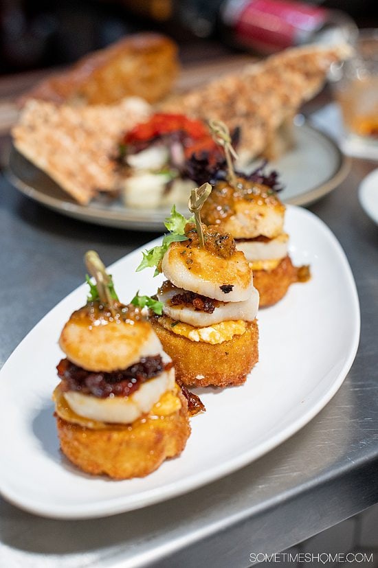 Plate of three scallops with bacon jam between each scallop, on a cheddar grit cake at The Kounter in Rock Hill, SC.